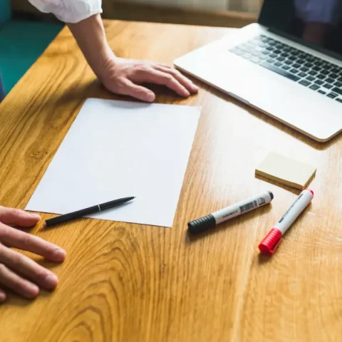 businessperson-s-hand-with-blank-white-paper-wooden-desk