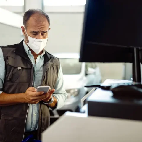 car-repairman-with-protective-face-mask-texting-smart-phone-his-workshop