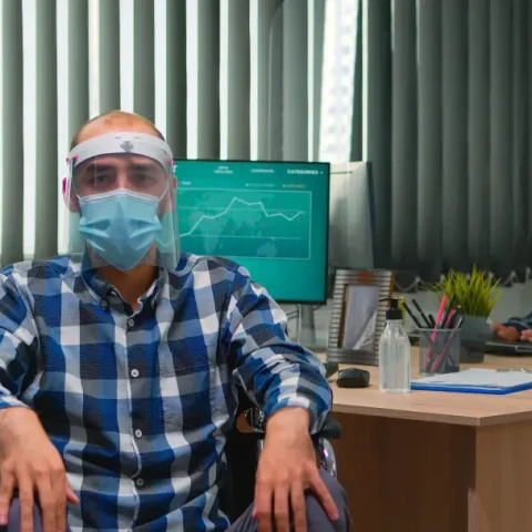 handicapped-businessman-wheelchair-with-mask-having-online-conference-business-office-covid-19-pandemic-immobilized-freelancer-working-financial-company-respecting-social-distance