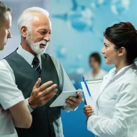 happy-mature-businessman-using-digital-tablet-while-talking-healthcare-workers-hallway-clinic